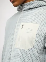 Campera de entrenamiento Umbro con capucha, cierre frontal completo y bolsillo en el pecho de nylon con cierre. Presenta una textura de tejido en relieve y logo de la marca estampado en el bolsillo.