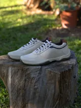 Championes urbanos de cuero color beige con detalles en marrón oscuro y azul marino. Presentan una textura microperforada en la puntera y laterales, cordones claros y suela de goma resistente.
