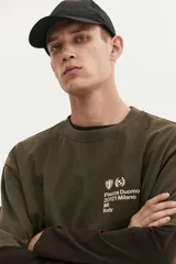 Remera de algodón de punto pesado con efecto lavado, color verde militar. Presenta un corte boxy (holgado) con cuello redondo ribeteado y un pequeño estampado blanco en el pecho con texto y logos.