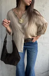 Camisa oversize color beige, con cuello redondo fruncido, cierre frontal de botones y mangas abullonadas con puños elásticos.
