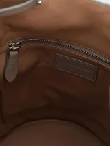 Bolso tipo bucket de cuero color beige con tachas plateadas en la parte inferior y doble asa de mano.