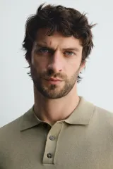 Polo de punto negro, manga corta, con cuello solapa y cierre frontal de tres botones. Presenta un calce regular y acabados en rib en mangas y ruedo.