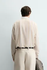 Camisa de corte relajado confeccionada en tejido fluido con mezcla de viscosa, presenta un diseño de rayas verticales en tonos neutros, cuello solapa, cierre frontal de botones y mangas largas con puños abotonados.
