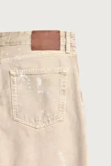 Jeans flare fit de tiro medio confeccionados en denim de algodón color beige, con cinco bolsillos, efecto salpicaduras y bajo irregular.
