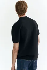 Remera polo de manga corta en punto texturizado negro, con cuello y tapeta de tres botones. Remate acanalado en puños y bajo, con un corte estándar.