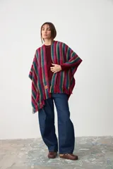 Ruana abierta de tejido de punto con diseño de rayas verticales en tonos fucsia, verde azulado y azul. Presenta terminaciones con flecos en el ruedo y una etiqueta de cuero sintético en el frente.