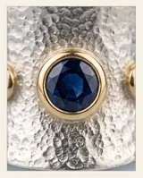 Anillo ancho de plata 925 con textura martillada y detalles en oro de 18k, incrustado con tres circonias azules.