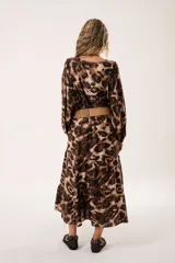 Vestido midi de corte holgado con estampado animal print en tonos marrones y beige. Tiene cuello redondo con lazo, mangas largas abullonadas y falda amplia con volantes. Incluye cinturón marrón con tachas.