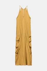 Vestido largo satinado color mostaza, con escote en pico y tirantes finos. Presenta un diseño drapeado en la parte frontal y bajo asimétrico, con cierre en la espalda con abertura y botón.