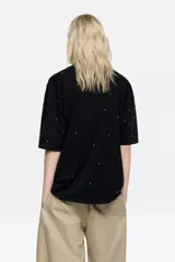 Remera de corte boxy en color negro, con escote redondo y manga corta recta. Presenta detalles de remaches metálicos distribuidos por toda la prenda.