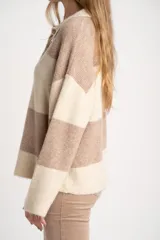 Sweater de tejido de punto color blanco roto o crema, con textura jaspeada. Presenta cuello polo y un escote con tres botones nacarados. El calce es holgado (oversize) y tiene mangas largas.