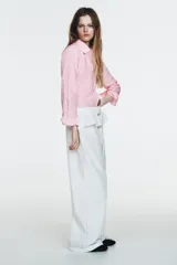 Pantalón blanco de nylon, tiro alto, con cintura elástica y detalle de sobrefalda o peplum superpuesto con hebilla metálica. Corte ancho y pierna recta.