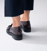 Mocasín de cuero vacuno negro con detalle de pieza de cuero con textura de cocodrilo y hebillas metálicas. Suela de caucho con plataforma.