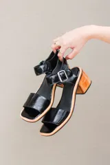 Sandalias negras de cuero charol, con tira ancha sobre los dedos y tobillo con hebilla metálica. Taco de madera.