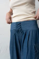 Pantalón estilo babucha color azul, de corte ancho con pretina ancha fruncida y cordones cruzados al frente. Cuenta con bolsillos cargo laterales y botamangas ajustables.