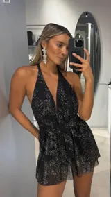 Mono corto de fiesta color negro con estampado de puntos brillantes plateados, escote halter profundo y diseño con volados en la parte inferior.