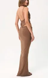 Vestido largo color marrón, de corte ajustado, con escote drapeado y tirantes finos. Presenta un diseño con abertura lateral en la cintura y detalle de fruncido en la falda.
