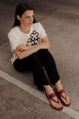 Sandalia plana de cuero color rojo, estilo chinela, con tiras finas adornadas con microtachas doradas. Posee tira de sujeción al tobillo con hebilla.