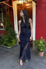 Falda larga de color azul marino confeccionada en microtul y gasa. Presenta un diseño con frunces y plisados en la zona de la cadera que brindan un ajuste al cuerpo, y una parte inferior fluida con transparencias y efecto godet.