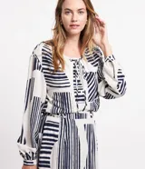 Camisa amplia de viscolino con estampado geométrico en azul marino sobre fondo crudo. Tiene cuello redondo con lazo, mangas largas abullonadas y abotonadura frontal.