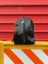 Mochila negra con textura símil cuero de cocodrilo, con bolsillo vertical delantero con cierre y bolsillo oculto en la espalda.