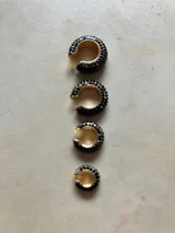 Set de tres aros trepadores con brillos, uno en tono bronce con piedras negras, uno dorado con piedras transparentes y uno plateado con piedras transparentes.