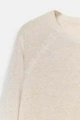 Jersey de punto color gris claro con hilo metalizado, de cuello redondo y manga larga. Bajo recto con aberturas laterales.