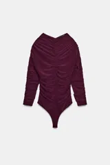 Body de manga larga con cuello en pico y diseño completamente fruncido. Presenta cierre inferior con botones a presión.