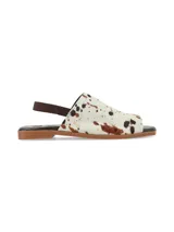 Sandalia plana Isotta de cuero con pelo, con estampado animal print tipo vaca en tonos blanco, marrón y negro. Cuenta con elástico trasero marrón y suela plana.