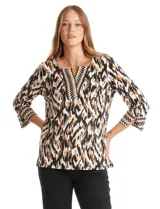 Blusa de algodón con estampado ikat en tonos blanco, negro y marrón. Presenta cuello a la base con escote en V y un patrón geométrico bordado. El estampado se realza con sutiles tachas doradas. Mangas tres cuartos con puño ancho y pequeña abertura lateral. Ruedo con tajos en los costados.