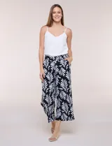 Pantalón crop de lino y rayón marca Dash, con estampado de hojas en blanco sobre fondo negro. Presenta tiro medio, pretina elástica en la parte trasera y bolsillos frontales.