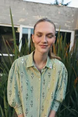 Camisa de corte recto en color verde claro con estampado de rayas verticales y detalles de lentejuelas brillantes. Presenta cuello solapa, cierre frontal con botones y mangas tres cuartos.