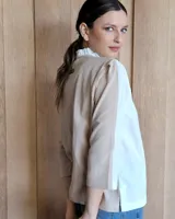 Camisa de manga tres cuartos color beige con cuello con volados y botones frontales. Presenta un detalle de color negro en la parte superior de las mangas.