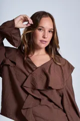 Blusa de color marrón con escote en V, mangas largas abullonadas con puños elásticos y detalles de volados en los hombros y el frente.