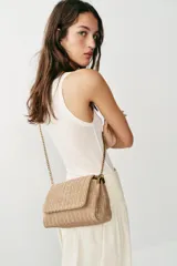 Bolso de hombro formato bandolera con cuerpo en efecto trenzado de color beige. Cuenta con asa de hombro combinada de cadena metálica dorada y tira de cuero sintético marrón, compartimento interior con cremallera y cierre mediante botón imantado.