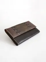 Billetera de cuero con diseño bicolor en tonos marrón y chocolate, presenta detalles de costuras decorativas en forma de cruces en la solapa frontal y cierre con broche.