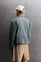 Chaqueta técnica de corte relajado, confeccionada en tejido compacto y elástico. Presenta cuello y puños acabados en rib, cierre frontal con cremallera, bolsillos frontales con cremallera oculta y bajo ajustable con elástico en los laterales.