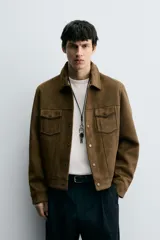 Cazadora de hombre de corte regular fit, color marrón oscuro, confeccionada en tejido efecto ante. Presenta cuello solapa, manga larga con puño abotonado, dos bolsillos de plastrón con solapa en el pecho y bolsillos laterales en la costura de la cadera. Cierre frontal con botones a presión.