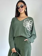 Sweater de punto oversized color verde, con escote en V y manga larga. Presenta un aplique bordado en forma de flor en el hombro izquierdo.