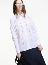Camisa blanca de algodón con cuello camisero, cierre frontal con botones y apliques de cadenas plateadas.
