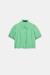 Camisa corta de cuello solapa y manga corta abullonada acabada en elástico, color verde con estampado de cuadros vichy. Cuenta con un bolsillo de plastrón en el delantero, bajo con elástico y cierre frontal con botones.