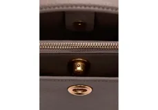 Bolso de mano tipo bucket pequeño en color marrón topo, con asa superior fija y detalle de aplique metálico circular dorado en el centro.