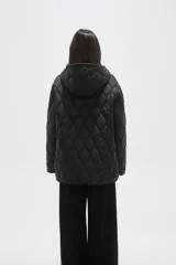 Campera acolchada de color negro con diseño capitoneado de ondas, manga larga, capucha integrada y cierre frontal con botones a presión.