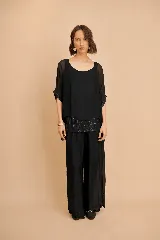 Conjunto negro de dos piezas que incluye una remera holgada de cuello redondo con mangas cortas y detalles de lentejuelas, y un pantalón largo de corte amplio y fluido.