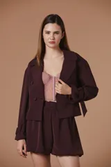 Saco corto de corte sastrero en color bordó, con solapas clásicas, cierre frontal de doble botonadura y mangas largas con detalle de lazos ajustables en los puños.