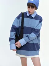 Buzo tejido de corte oversize con diseño de rayas horizontales en tonos azul y celeste. Presenta cuello redondo, hombros caídos y terminaciones acanaladas en puños y bajo.