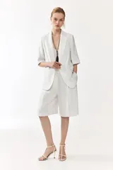 Blazer de botonadura sencilla con solapas de muesca, color blanco, de manga corta, con cierre de un botón y bolsillos delanteros ribeteados, con forro interno en tono tostado.