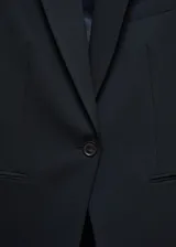Blazer entallado de color negro, con solapas con muesca, hombros estructurados y cierre frontal de un botón. Presenta dos bolsillos de ribete delanteros, pinzas de entalle y una abertura posterior.