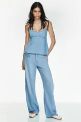 Pantalón de jean estilo pijamero de tiro medio, con cintura elástica ajustable mediante cordones. Presenta corte recto, bolsillos laterales y cierre frontal con cremallera y gancho metálico.