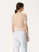 Top de tejido crochet color beige, con cuello redondo y mangas cortas con terminación ondulada.